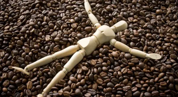 Holzfigur liegt auf einem Berg gerösteter Kaffeebohnen. Sieht aus, als würde sie die Kaffeebohnen kauen.