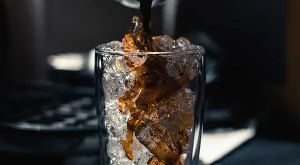 Heißer Espresso fließt auf Eiswürfel in einem Glas. Perfekt für ein erfrischendes iced americano rezept.