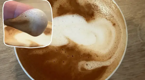 Ein Finger berührt den cremigen milch schaum eines Kaffees. Die Latte Art ist kunstvoll in den braunen Kaffee gemalt.