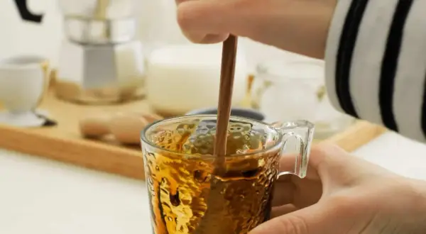 Eine Hand rührt mit einem Holzstäbchen in einem Glas Kaffee. Perfekt für die Kaffeesirup Verwendung für süße Kaffeekreationen.