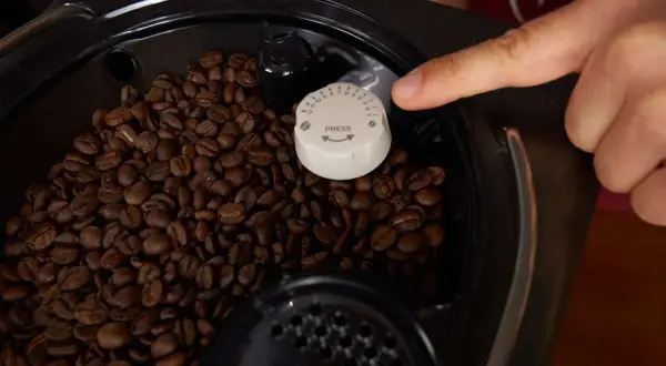 Finger stellt den Mahlgrad am Kaffeevollautomaten ein. Zahlreiche Kaffeebohnen sind im Behälter sichtbar.