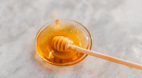 Ein Honiglöffel in einer Schale mit flüssigem Honig, der an den süßen Geschmack von Honey Process Kaffee erinnert.