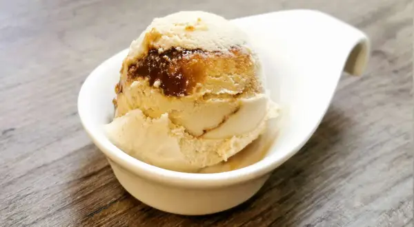 Cremiges Eis mit Karamellsauce, das an einen iced macchiato erinnert, in einer weißen Schale auf Holztisch.