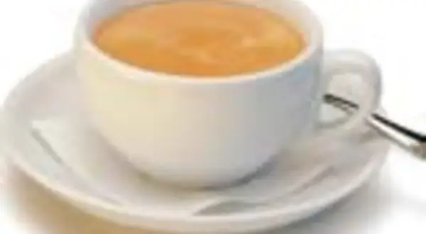 Eine Tasse mit cremigem, braunem Kaffee steht auf einer Untertasse. Ein kleiner Löffel liegt daneben.