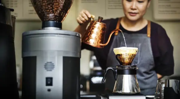 Barista bereitet mit einem Handfilter und einer Kupferkanne einen aromatischen Espresso zu.