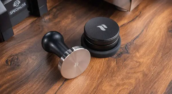 Ein Tamper ist ein Werkzeug zum Verdichten von Kaffeepulver im Siebträger. Hier liegt ein schicker Tamper neben einem Kaffee-Dosierring.