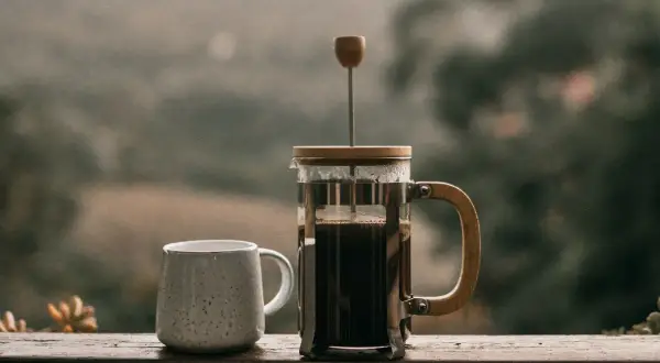 Eine French Press, bereit für den perfekten Kaffee. Neben einer Tasse wartet sie auf den Genuss.