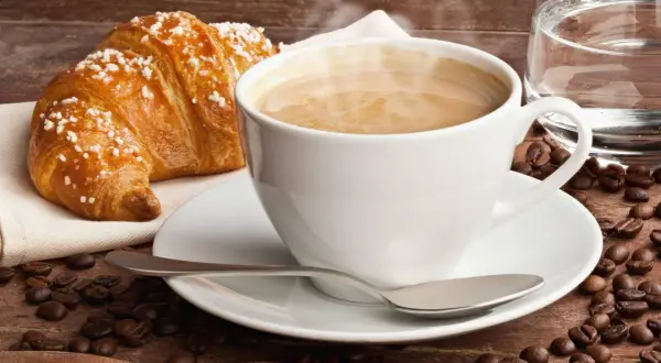 Dampfender Cappuccino mit Croissant und Kaffeebohnen. Ein Genuss, der die **Cappuccino Kalorien** wert ist.