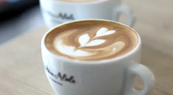Zwei Tassen mit Latte Art, bereit zum Cappuccino trinken. Ein Herzmuster ziert den Schaum.