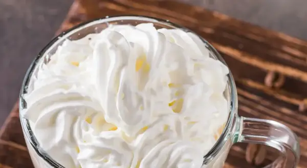Ein Glas mit cremigem Cappuccino con panna, bedeckt mit einer üppigen Haube aus Schlagsahne.