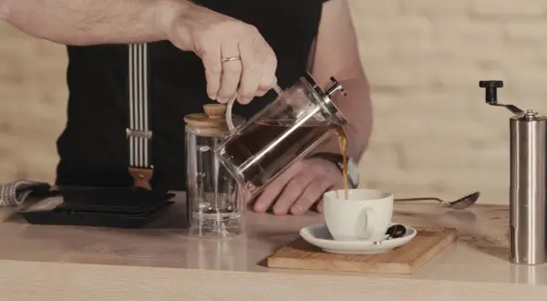 Mann gießt French Press Kaffee in eine Tasse. Die Menge ist für 2 Tassen ausgelegt.