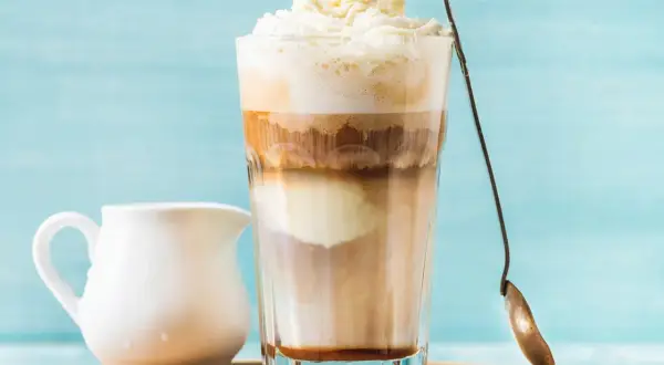 Ein cremiger Eiskaffee Karamell mit Sahnehaube, daneben ein Milchkännchen.