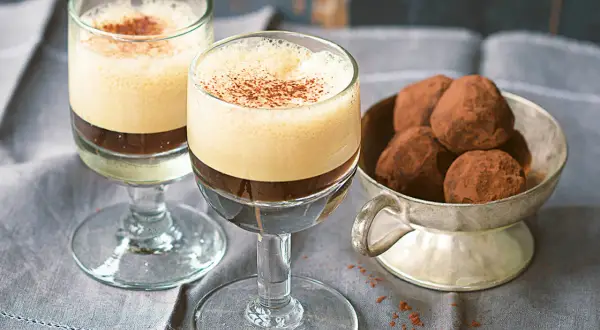 Zwei Gläser mit cremigem Caffe Shakerato, bestäubt mit Kakao. Daneben eine Schale mit Schokoladentrüffeln.