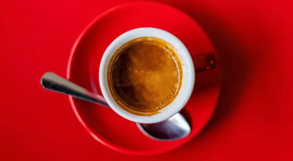 Eine Tasse Espresso auf rotem Untergrund. Die Wirkung von Espresso auf den Schlaf ist oft belebend, nicht schlaffördernd.