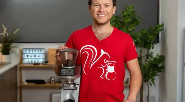 Mann in rotem T-Shirt mit Eichhörnchen-Aufdruck hält Kaffeemühle, bereit für perfekten Ristretto ml.