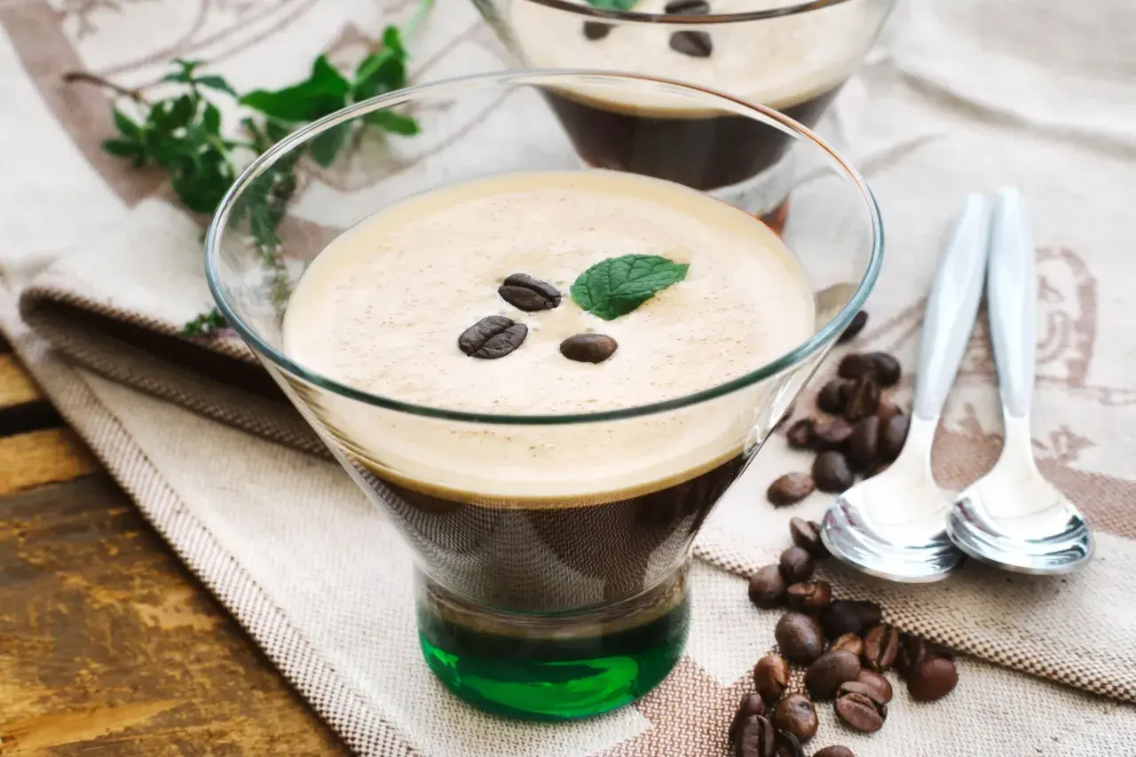 Ein köstlicher Eiskaffee italienisch, garniert mit Kaffeebohnen und Minze, serviert in einem Glas mit grüner Likörschicht.