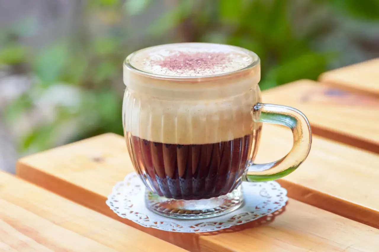 Ein Glas mit cremigem Kaffee mit Ei, bestäubt mit Kakao, steht auf einem Holztisch.
