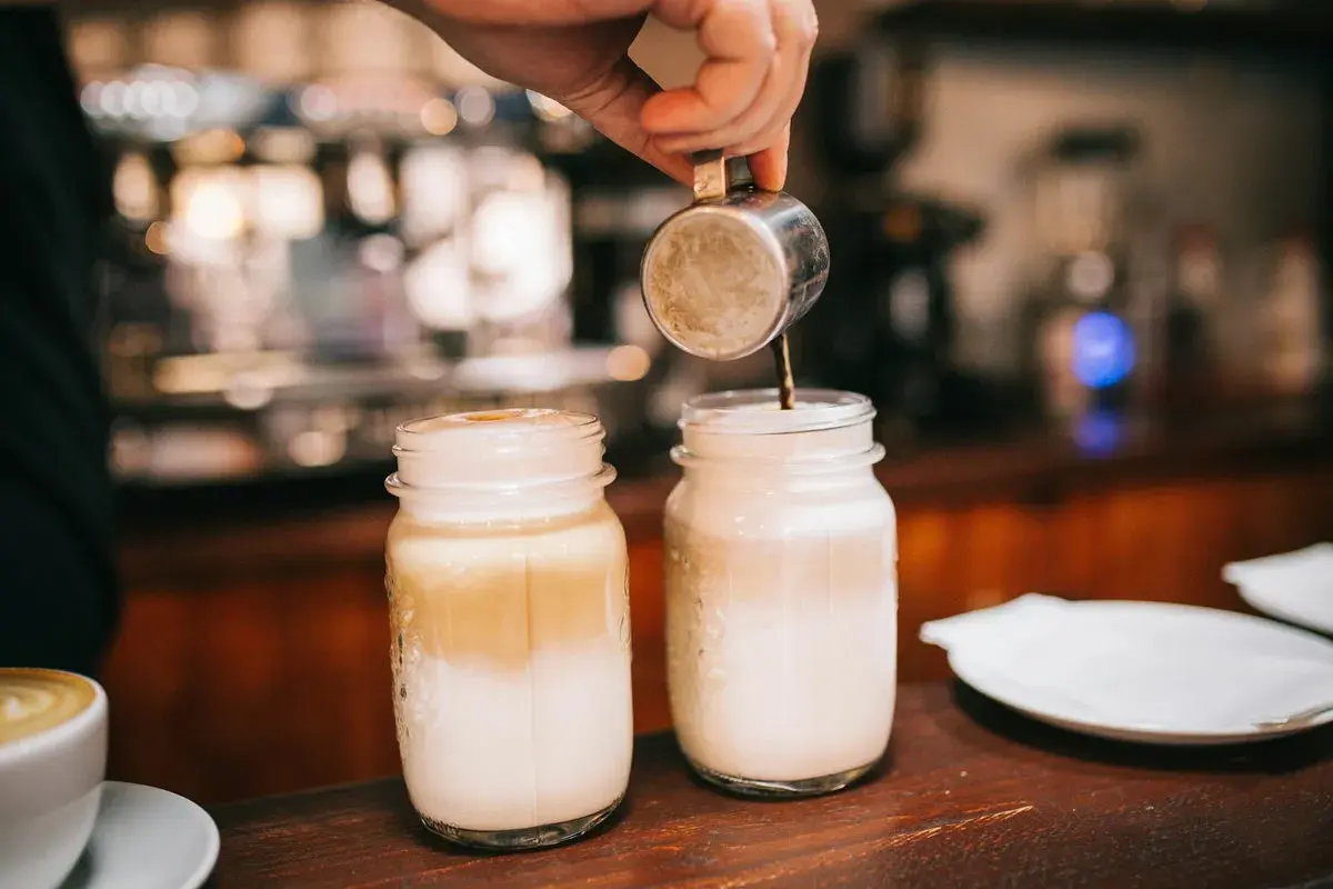 Zwei Latte Macchiato in Gläsern, ein Barista gießt Espresso ein. Kalorienbewusst genießen?