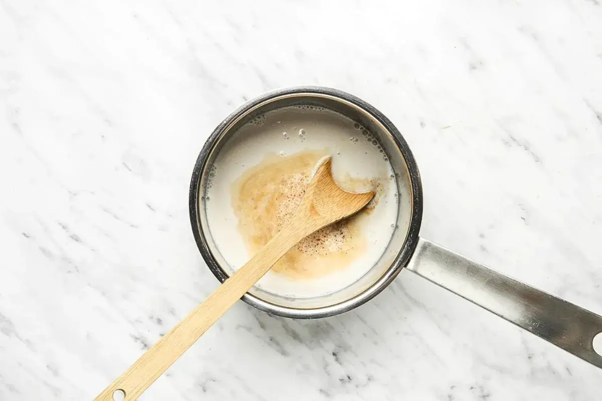 Ein Holzlöffel rührt in einem Topf mit cremiger Hafermilch, die für einen köstlichen Hafermilch-Latte vorbereitet wird.