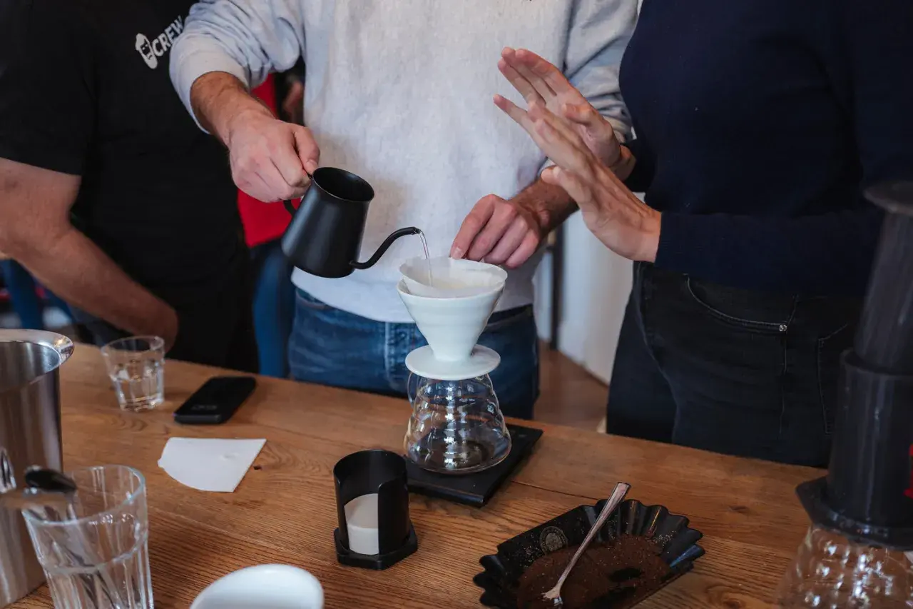 Hände bereiten Kaffee zu, die **Koffeinwirkung** wird bald spürbar sein. Wasser fließt in einen Filter über einer Karaffe.