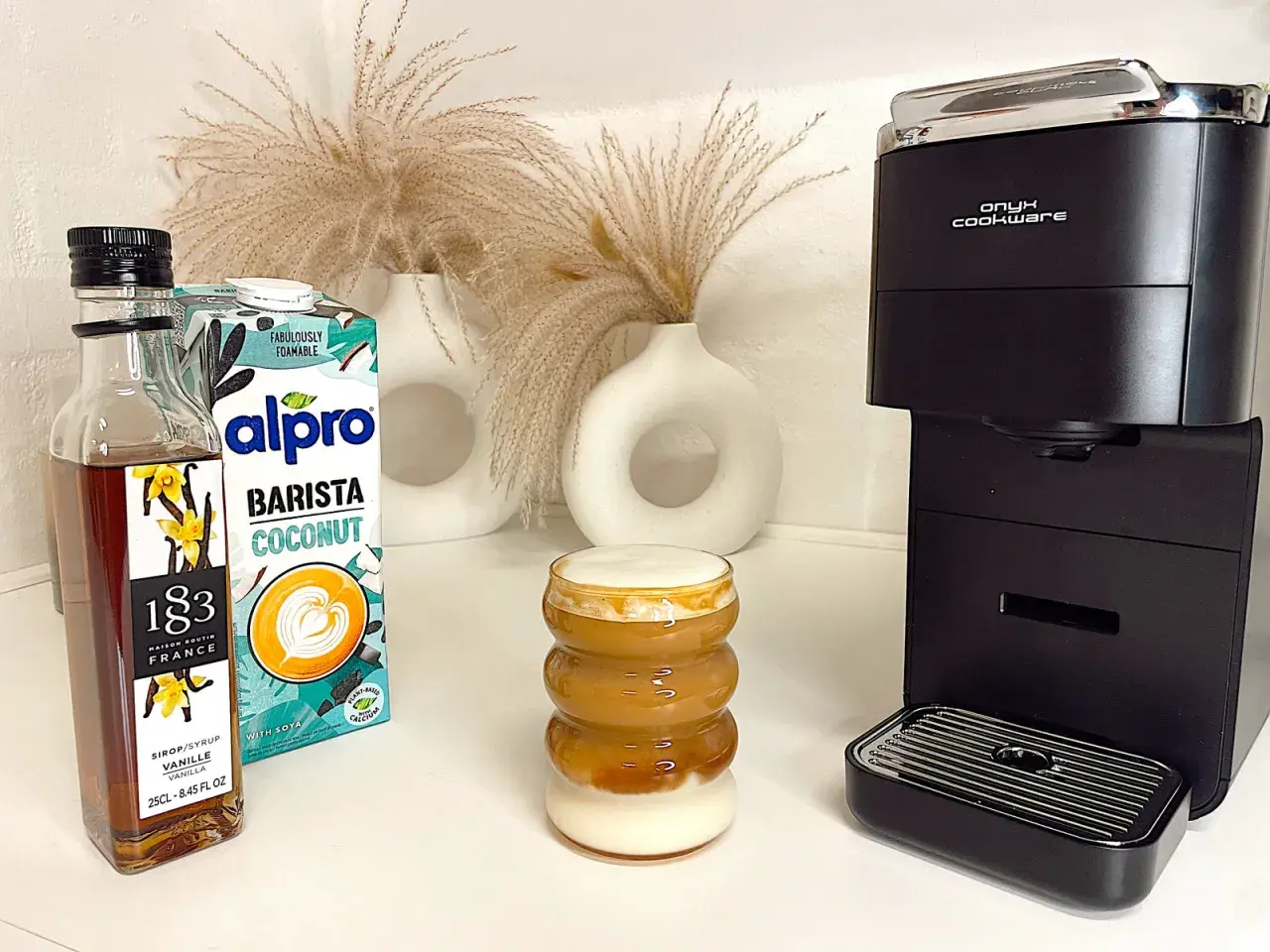 Ein leckerer Kokosnuss-Latte mit Alpro Barista Coconut, Vanillesirup und einer Kaffeemaschine.