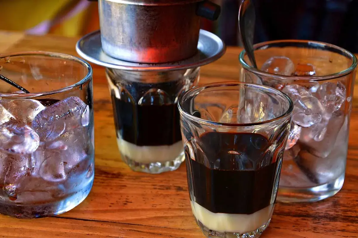 Zwei Gläser mit süßer Kondensmilch und starkem Kaffee, bereit für Eiswürfel. Ein vietnamesischer Eiskaffee zum Genießen.