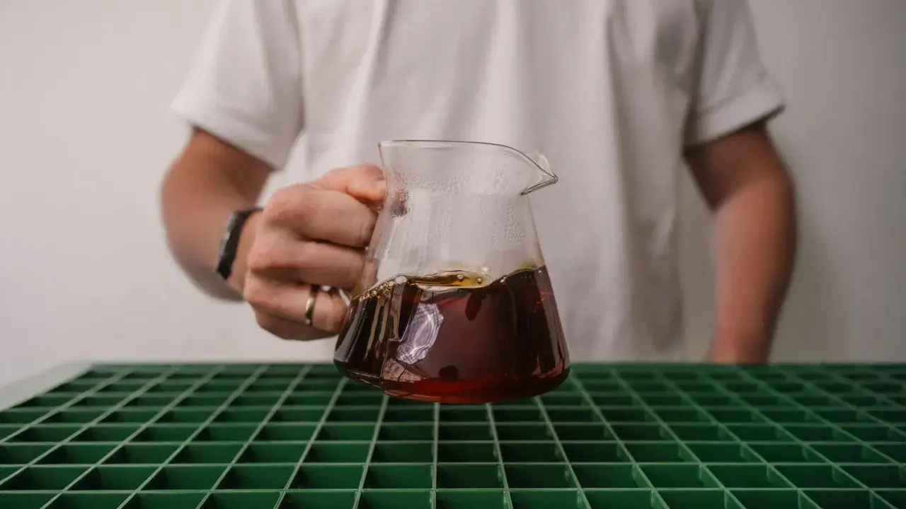 Person hält ein Glasgefäß mit frisch gebrühtem Kaffee, der gerade extrahiert wurde.