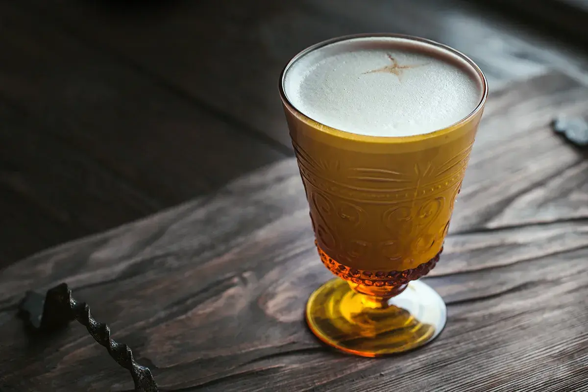 Ein goldener Becher mit cremigem Schaum, der an einen russischen Kaffee erinnert, steht auf einem rustikalen Holztisch.