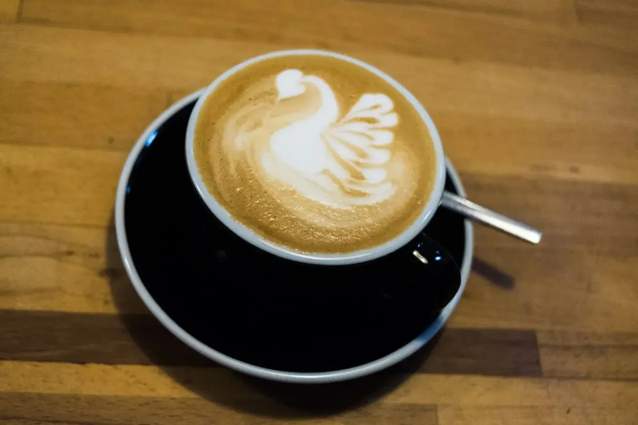 Kaffee mit einem Schwan aus Milchschaum zubereitet, serviert auf einem schwarzen Unterteller.