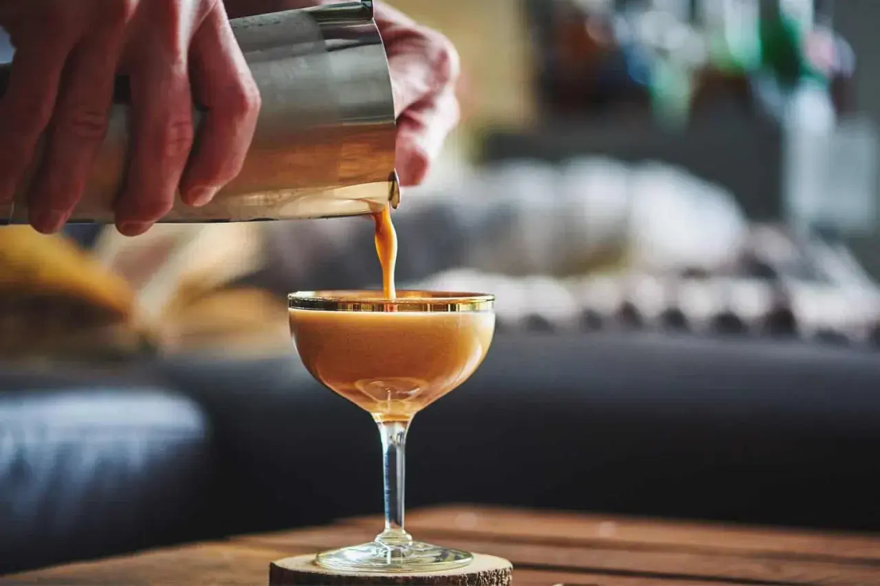 Ein cremiger Kaffee mit Alkohol wird aus einem Shaker in ein Glas gegossen. Ein köstlicher Kaffee-Cocktail, der zum Genießen einlädt.