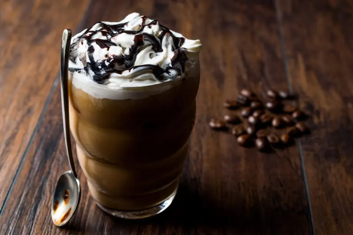 Eisgekühlter Kaffee mit Sahne und Schokoladensauce, ein köstliches Frappuccino Rezept. Daneben liegen geröstete Kaffeebohnen.