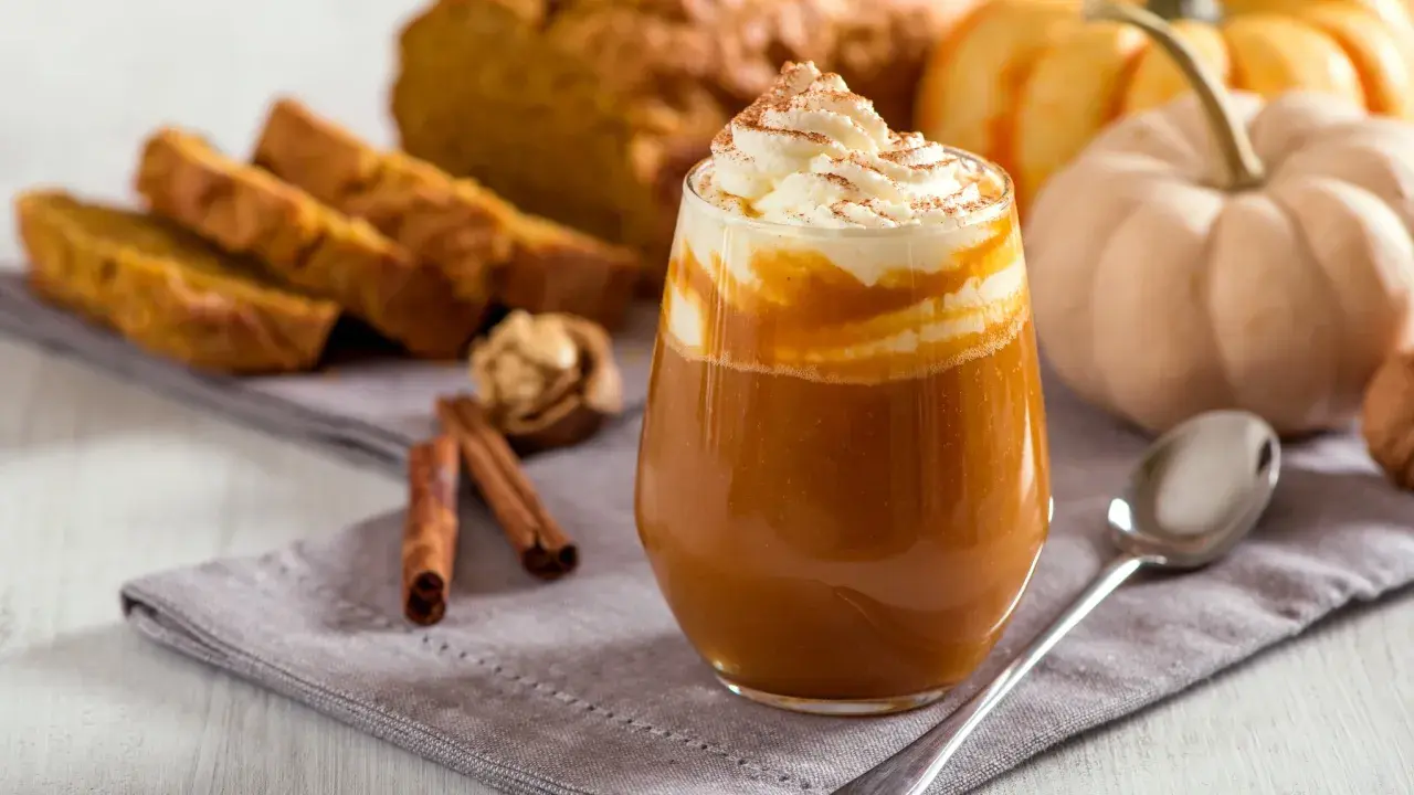 Ein cremiger Pumpkin Spice Latte mit Sahne und Zimt, daneben Kürbisbrot und Zimtstangen. Ein Genuss, der die pumpkin spice latte kalorien vergessen lässt.
