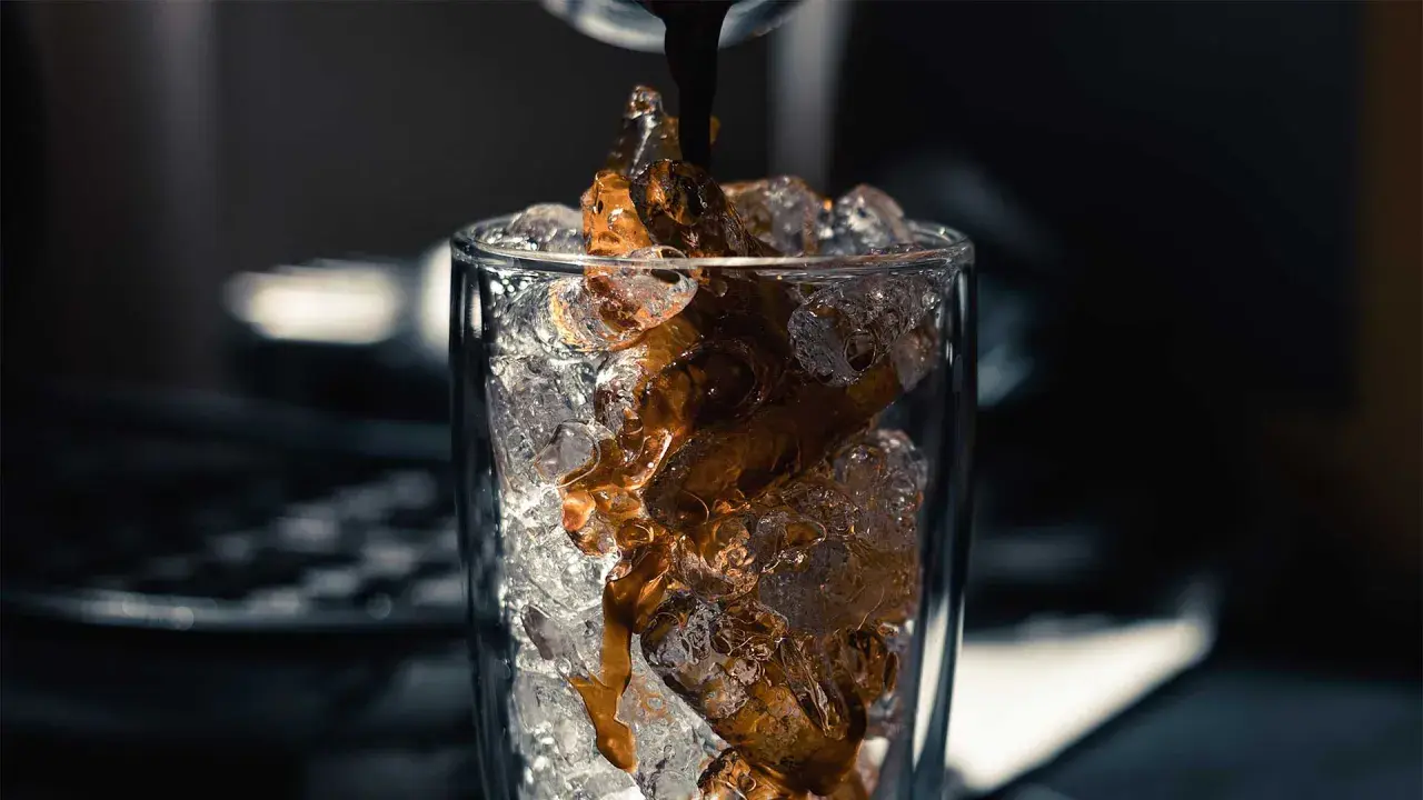 Heißer Espresso fließt auf Eiswürfel in einem Glas. Perfekt für ein erfrischendes iced americano rezept.