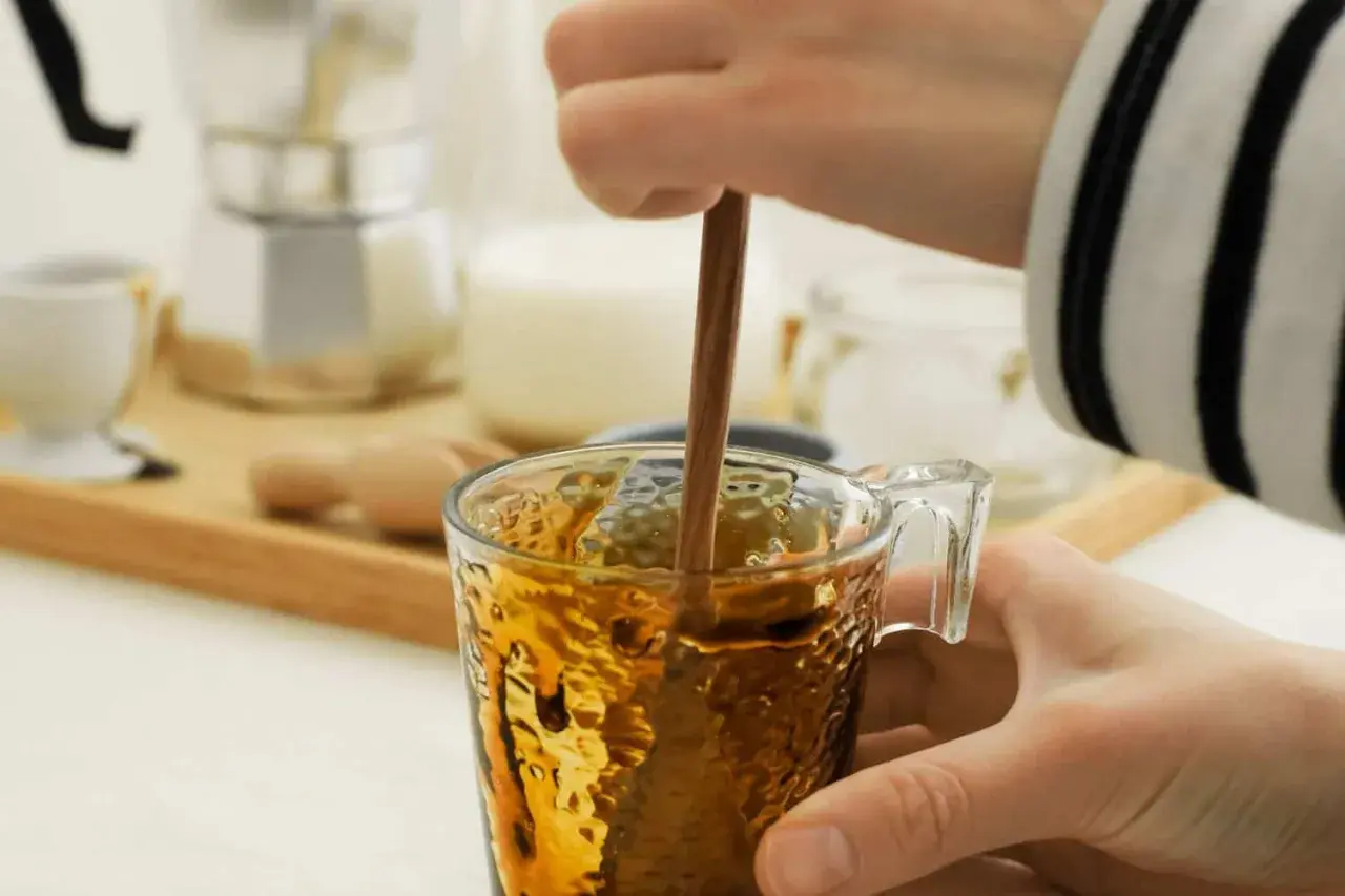 Eine Hand rührt mit einem Holzstäbchen in einem Glas Kaffee. Perfekt für die Kaffeesirup Verwendung für süße Kaffeekreationen.
