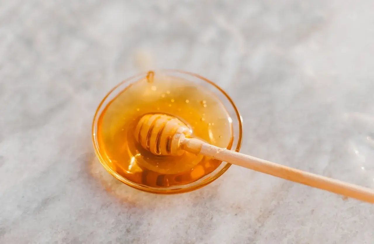 Ein Honiglöffel in einer Schale mit flüssigem Honig, der an den süßen Geschmack von Honey Process Kaffee erinnert.