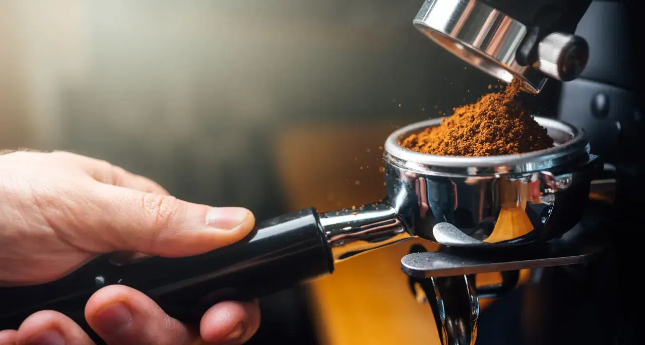 Frisch gemahlener Kaffee für den perfekten espresso geschmack. Eine Hand hält den Siebträger, während feines Kaffeepulver hineinfällt.