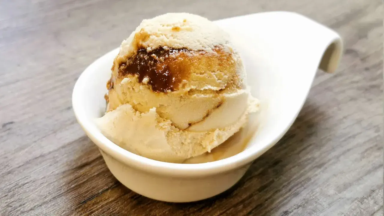 Cremiges Eis mit Karamellsauce, das an einen iced macchiato erinnert, in einer weißen Schale auf Holztisch.