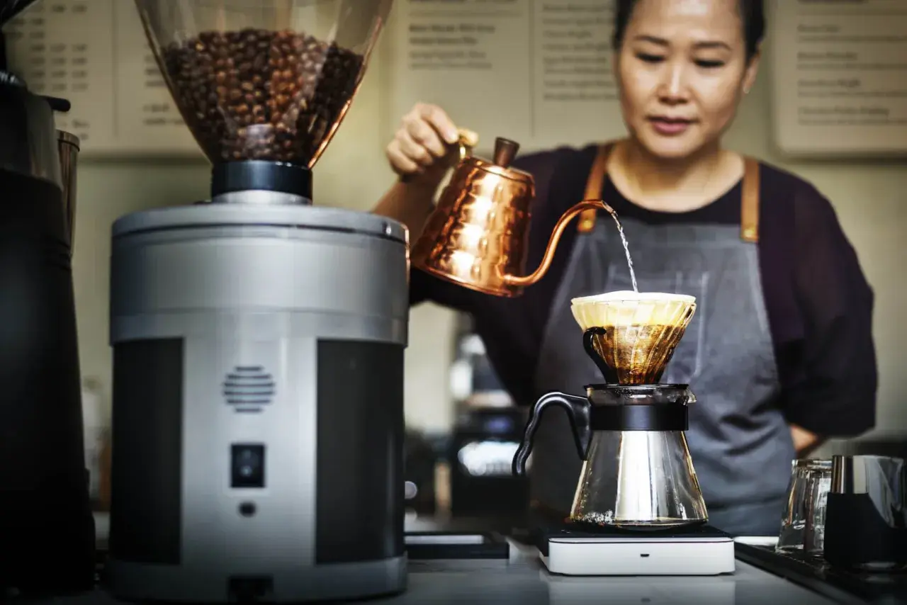 Barista bereitet mit einem Handfilter und einer Kupferkanne einen aromatischen Espresso zu.