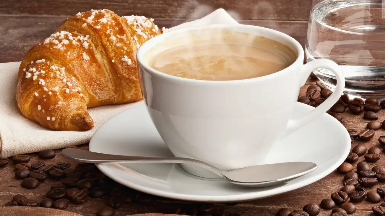 Dampfender Cappuccino mit Croissant und Kaffeebohnen. Ein Genuss, der die **Cappuccino Kalorien** wert ist.