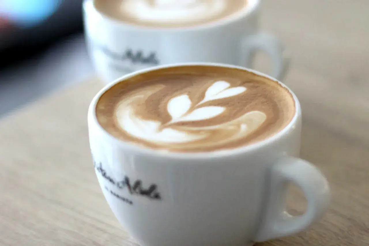 Zwei Tassen mit Latte Art, bereit zum Cappuccino trinken. Ein Herzmuster ziert den Schaum.