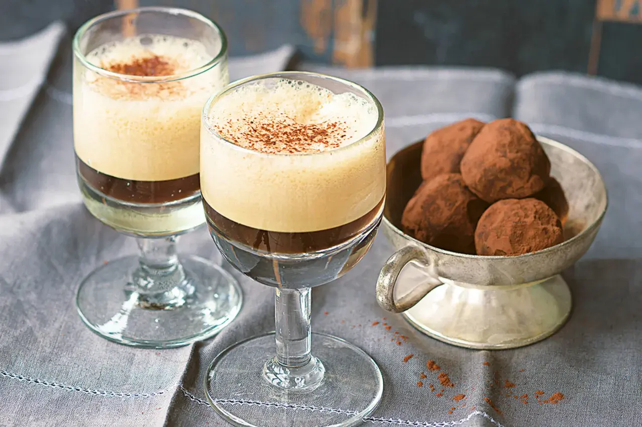Zwei Gläser mit cremigem Caffe Shakerato, bestäubt mit Kakao. Daneben eine Schale mit Schokoladentrüffeln.