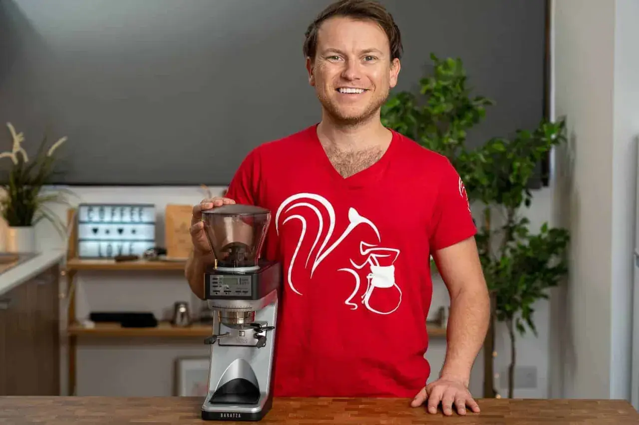 Mann in rotem T-Shirt mit Eichhörnchen-Aufdruck hält Kaffeemühle, bereit für perfekten Ristretto ml.