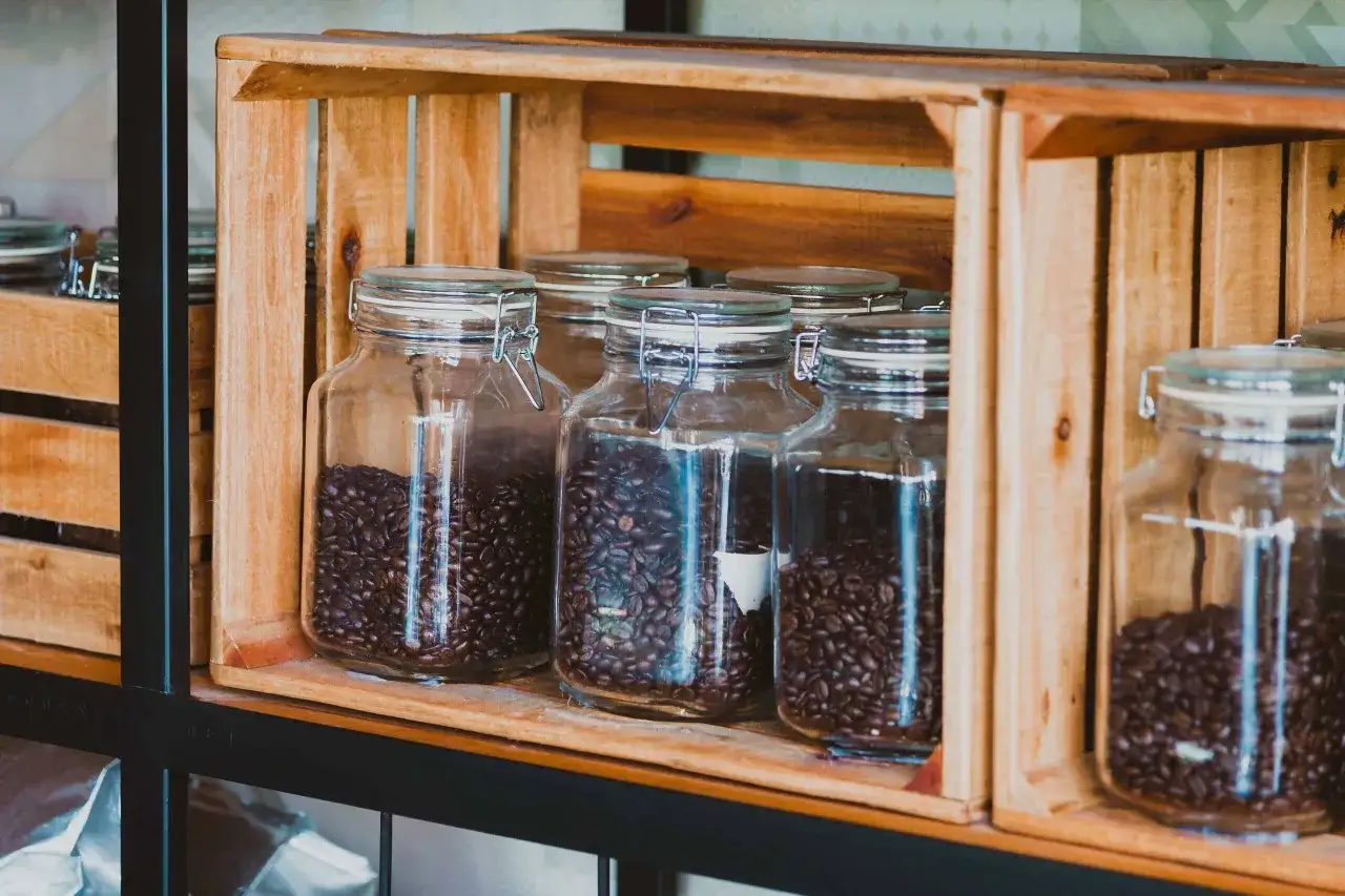 Mehrere Glasbeh&auml;lter mit Kaffeebohnen stehen in Holzkisten. Die Bohnen lagern frisch und duftend f&uuml;r den perfekten Morgenkaffee.