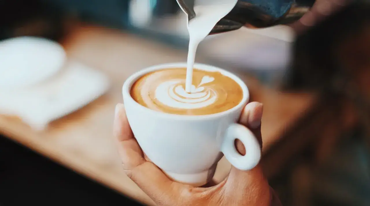 Barista verziert einen Cappuccino mit Milchschaum. Das ist die Kunst des Caf&eacute; Ol&eacute;.