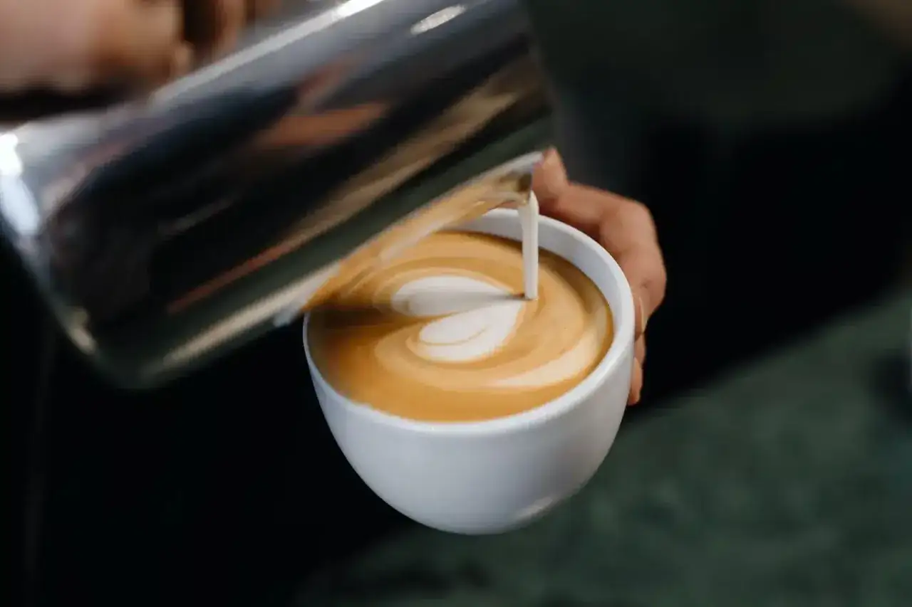 Barista gie&szlig;t Milch in Kaffee, um ein Latte Art Herz zu kreieren.