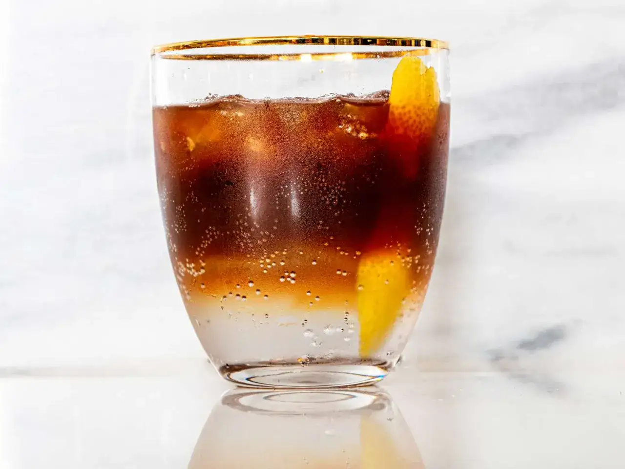 Erfrischender iced espresso mit Eiswürfeln und einem Zitronenzesten-Twist, serviert in einem eleganten Glas mit goldenem Rand.