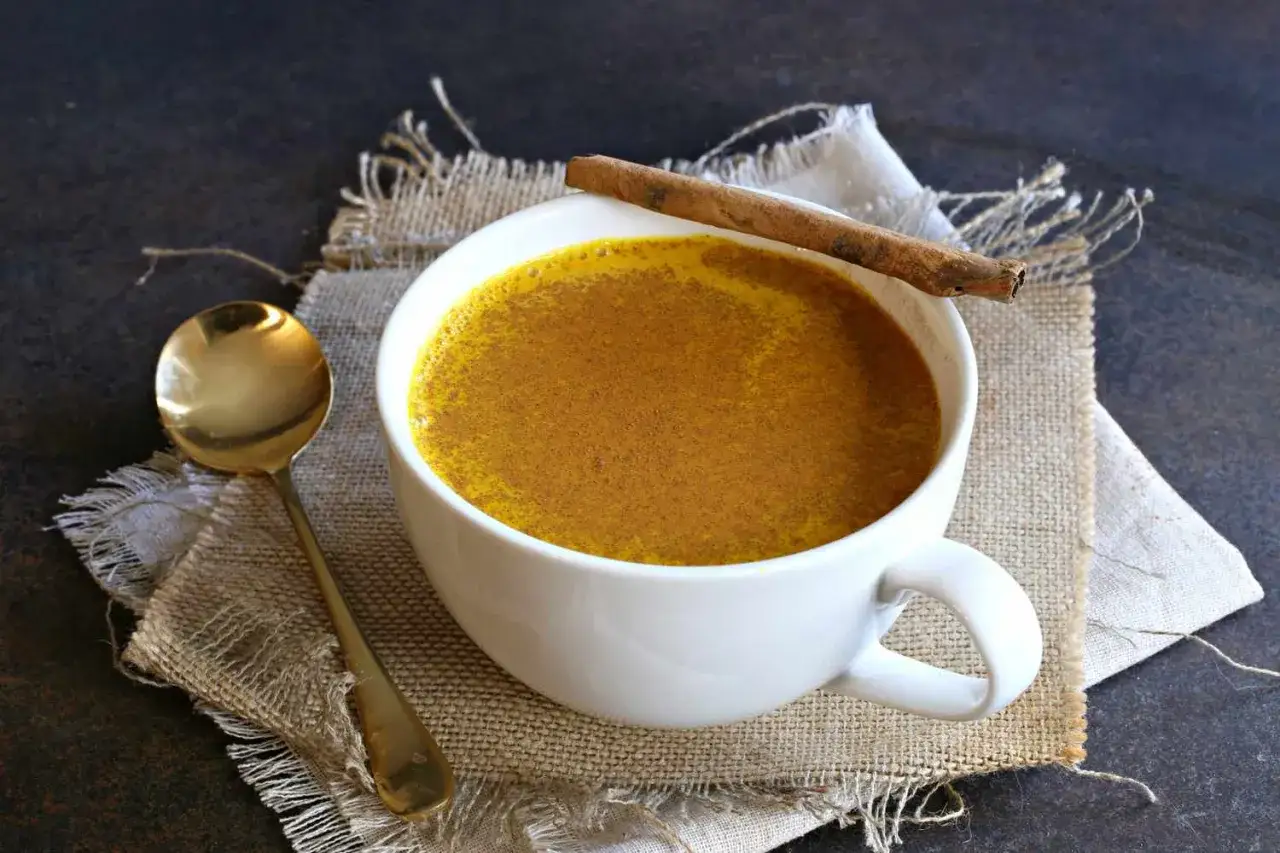 Eine Tasse goldener Kaffee mit Kurkuma und Zimtstange, daneben ein L&ouml;ffel.