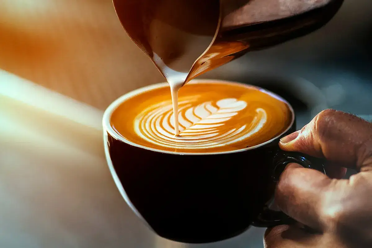 Barista gießt zarten milch schaum in eine Tasse Kaffee, um ein Latte Art Muster zu kreieren.