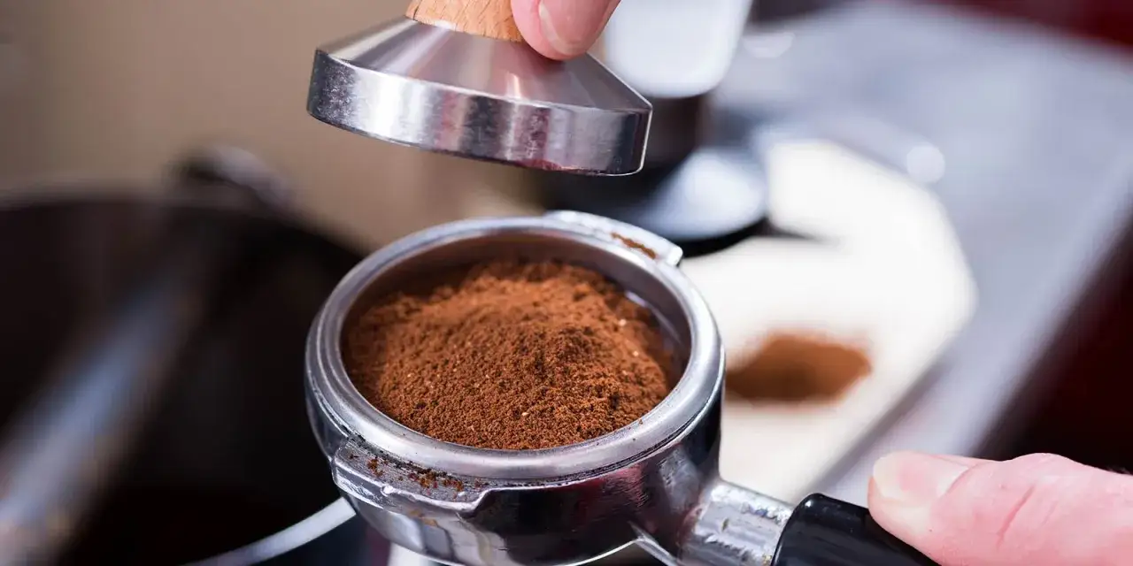 Ein Siebtr&auml;ger voller Kaffeepulver wartet darauf, mit einem Tamper verdichtet zu werden. So wird der perfekte Espresso zubereitet.