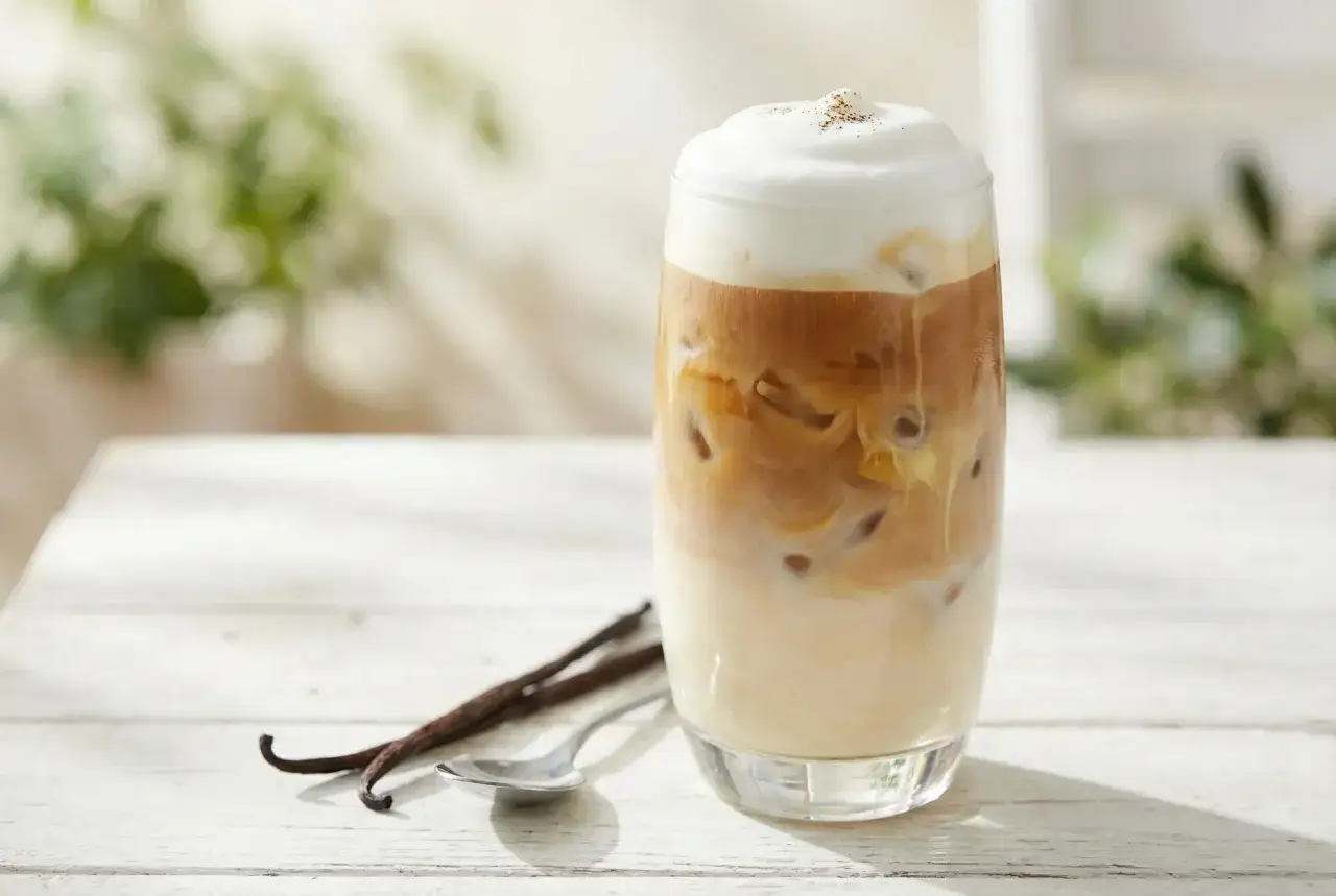 Ein erfrischender Latte Macchiato Eiskaffee mit cremigem Milchschaum und Vanilleschoten auf einem Holztisch.